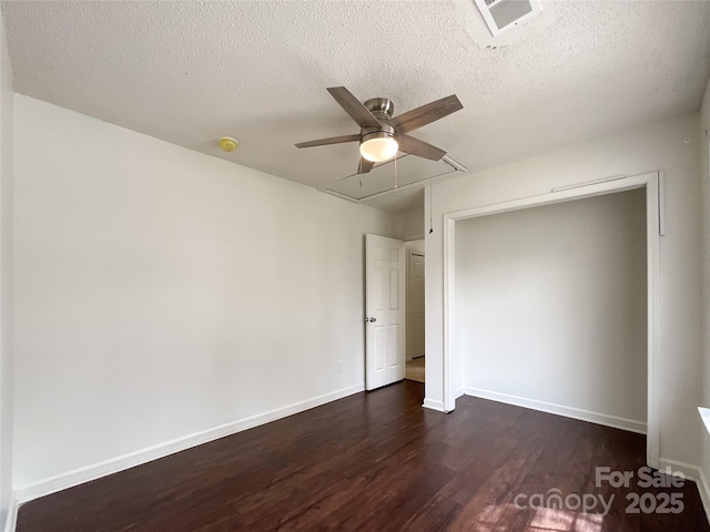 unfurnished bedroom featuring baseboards, attic access, ceiling fan, dark wood-type flooring, and a textured ceiling