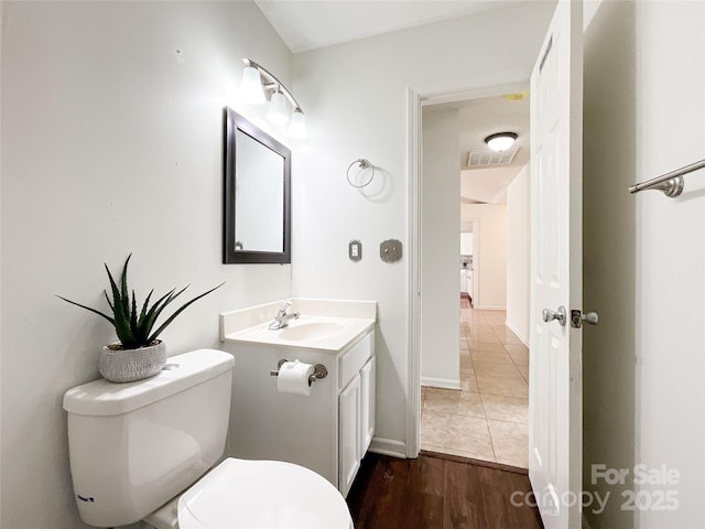 half bathroom with visible vents, toilet, wood finished floors, baseboards, and vanity