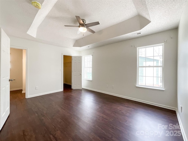 unfurnished bedroom with a tray ceiling, visible vents, dark wood-type flooring, and baseboards