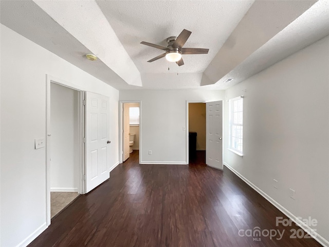 unfurnished bedroom with a textured ceiling, a raised ceiling, baseboards, and wood finished floors