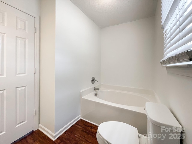 bathroom featuring baseboards, toilet, a garden tub, wood finished floors, and a textured ceiling