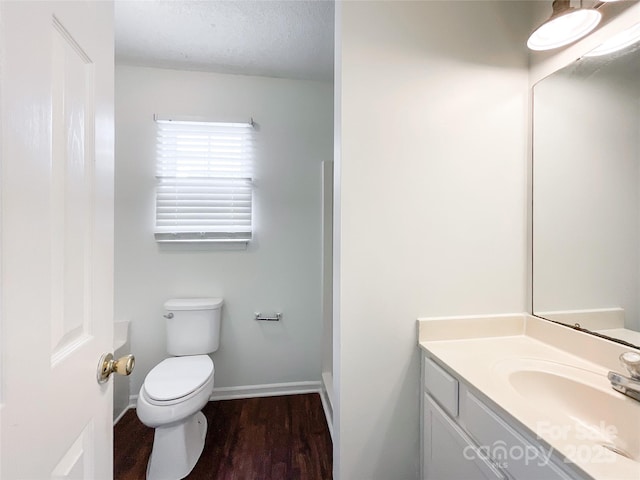 bathroom featuring toilet, a textured ceiling, wood finished floors, baseboards, and vanity