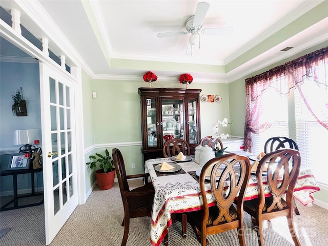 carpeted dining space with ornamental molding, a raised ceiling, ceiling fan, and french doors