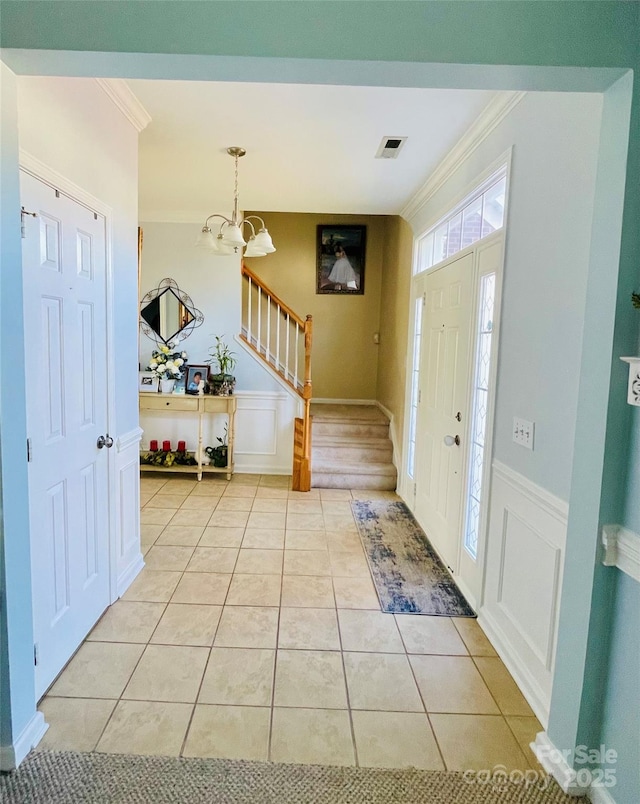 foyer entrance featuring light tile patterned floors, a notable chandelier, a wainscoted wall, ornamental molding, and stairway