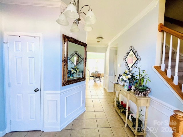 hall with light tile patterned floors, a chandelier, stairs, wainscoting, and crown molding