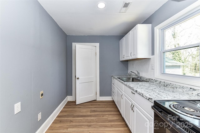 kitchen featuring wood finished floors, a sink, visible vents, white cabinets, and backsplash