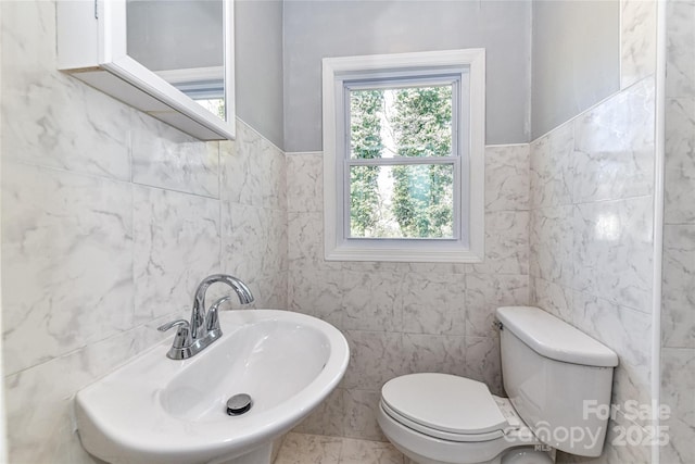 bathroom featuring a sink, tile walls, and toilet