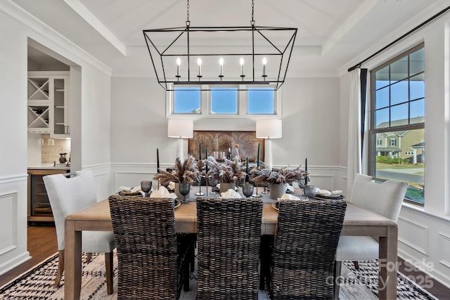 dining area with an inviting chandelier, a raised ceiling, wood finished floors, and a decorative wall