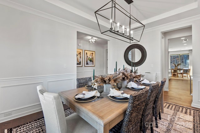 dining space featuring a chandelier, a wainscoted wall, wood finished floors, ornamental molding, and a raised ceiling