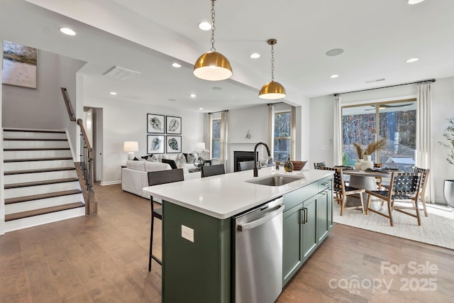 kitchen featuring dishwasher, decorative light fixtures, a kitchen island with sink, light countertops, and a sink