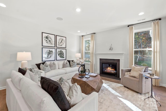 living area featuring recessed lighting, visible vents, light wood-style flooring, a fireplace with flush hearth, and baseboards