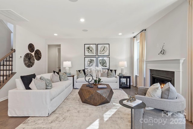 living room featuring a glass covered fireplace, wood finished floors, recessed lighting, and stairs