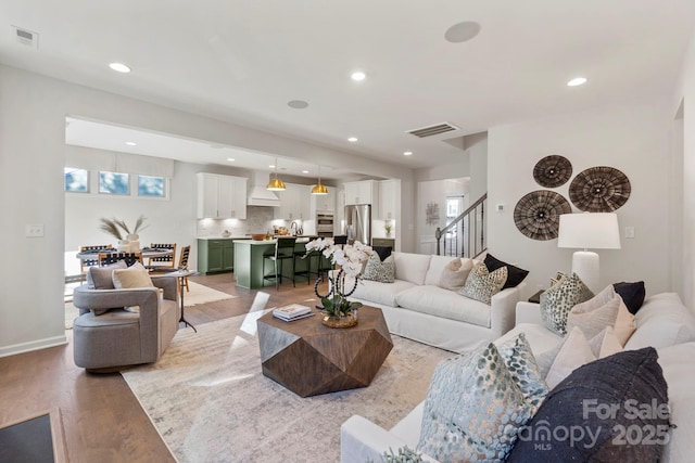 living room with stairs, light wood-style flooring, visible vents, and a healthy amount of sunlight