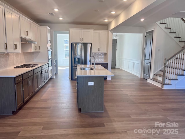 kitchen featuring appliances with stainless steel finishes, dark wood-style flooring, a sink, and a decorative wall