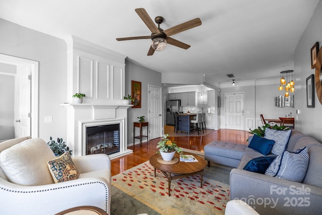 living area featuring a glass covered fireplace, wood finished floors, visible vents, and a ceiling fan