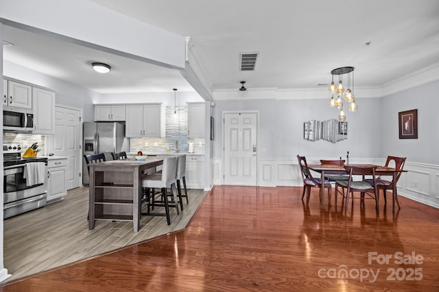 dining space featuring visible vents, wainscoting, ornamental molding, wood finished floors, and a decorative wall