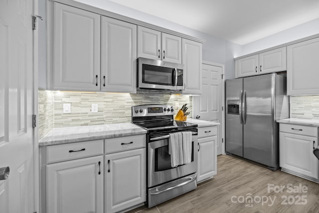 kitchen featuring appliances with stainless steel finishes, white cabinetry, light wood finished floors, and decorative backsplash