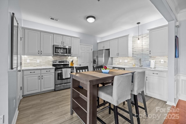 kitchen with light wood finished floors, visible vents, appliances with stainless steel finishes, decorative light fixtures, and a sink