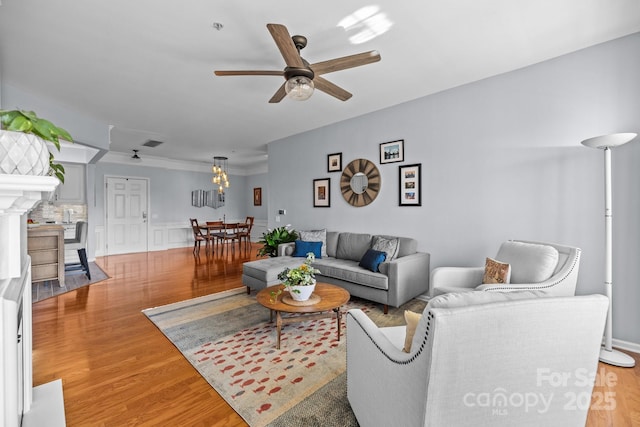 living area featuring ceiling fan, a wainscoted wall, light wood-type flooring, and visible vents