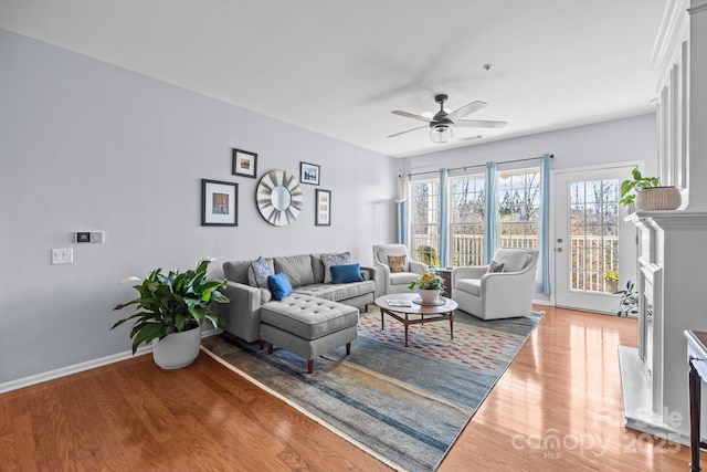 living area featuring a high end fireplace, baseboards, ceiling fan, and light wood finished floors