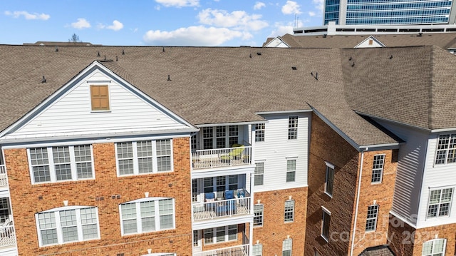 exterior space featuring brick siding and roof with shingles