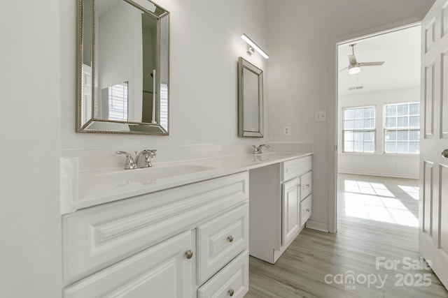 full bath with double vanity, wood finished floors, a sink, and a ceiling fan