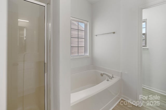 bathroom with a shower stall, baseboards, and a bath