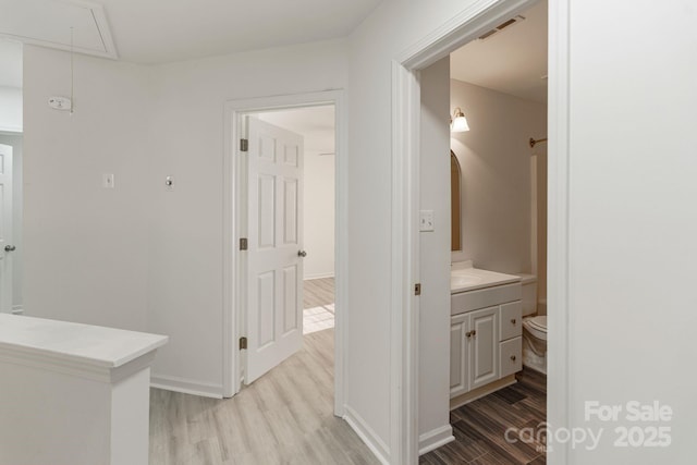 corridor with visible vents, attic access, a sink, light wood-type flooring, and baseboards