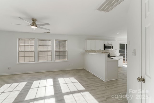 kitchen with visible vents, stainless steel microwave, white cabinets, range with electric cooktop, and a peninsula