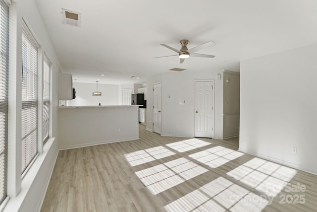 unfurnished living room featuring visible vents, light wood-type flooring, a ceiling fan, and baseboards