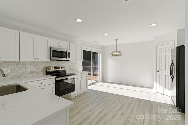 kitchen with light stone counters, pendant lighting, appliances with stainless steel finishes, white cabinetry, and a sink