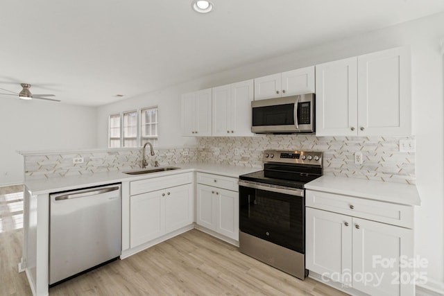 kitchen with a peninsula, a sink, white cabinetry, light countertops, and appliances with stainless steel finishes