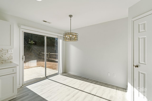 unfurnished dining area with a chandelier, visible vents, baseboards, and wood finished floors