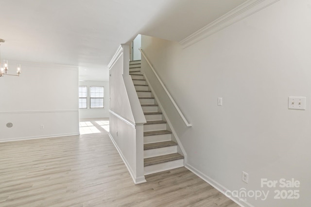 stairs featuring a notable chandelier, crown molding, baseboards, and wood finished floors