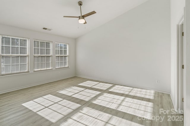 empty room with lofted ceiling, light wood finished floors, visible vents, and baseboards