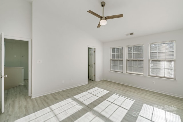 empty room with high vaulted ceiling, visible vents, light wood-style flooring, and baseboards