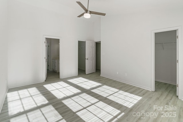 unfurnished bedroom with connected bathroom, a towering ceiling, light wood-style flooring, a spacious closet, and a closet