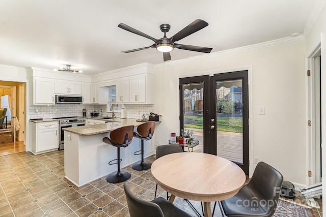 kitchen featuring a peninsula, a sink, white cabinets, appliances with stainless steel finishes, and light stone countertops