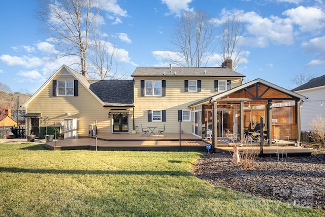 back of property with a chimney, roof with shingles, a yard, and a deck