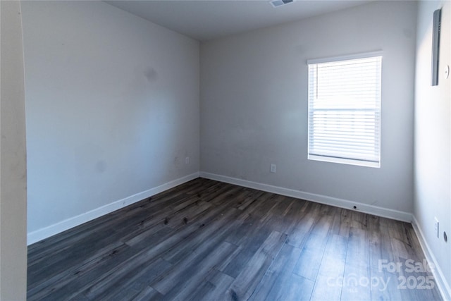 empty room with dark wood finished floors, visible vents, and baseboards