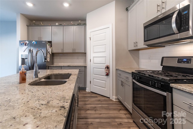 kitchen featuring light stone countertops, stainless steel appliances, a sink, and gray cabinetry