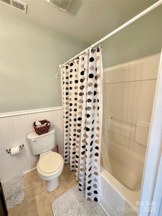 bathroom featuring visible vents, toilet, a wainscoted wall, shower / tub combo with curtain, and tile patterned floors