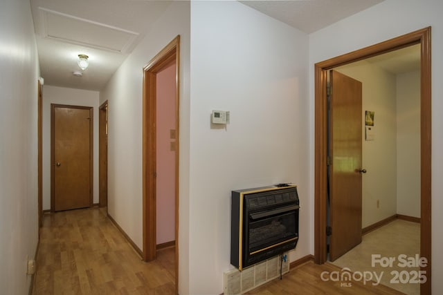 corridor with attic access, light wood-type flooring, baseboards, and heating unit