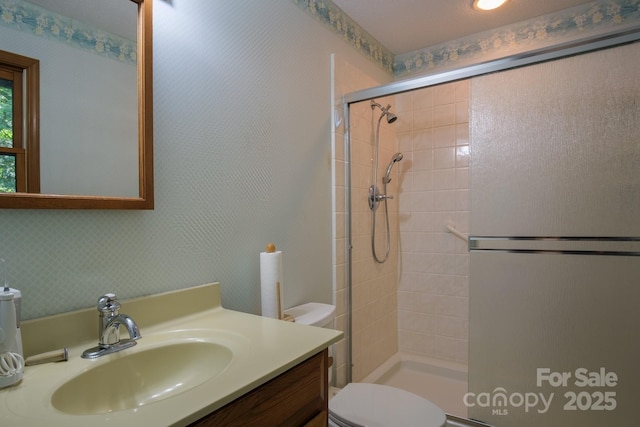 bathroom featuring tiled shower, vanity, toilet, and wallpapered walls