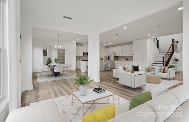 living area with light wood finished floors, visible vents, an inviting chandelier, stairs, and recessed lighting