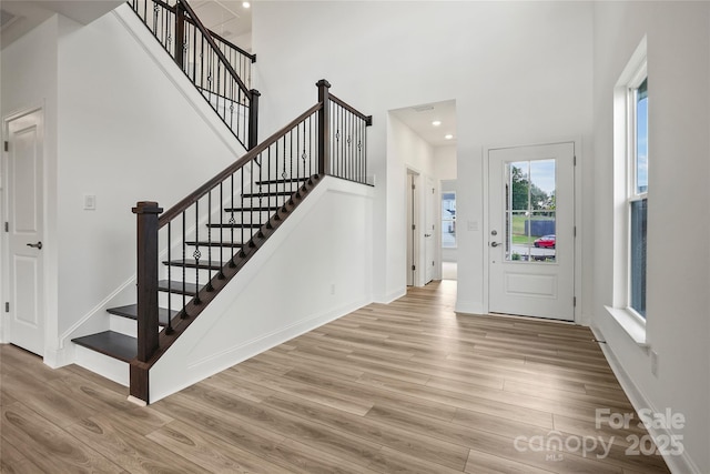 foyer entrance with a towering ceiling, light wood-style floors, and baseboards