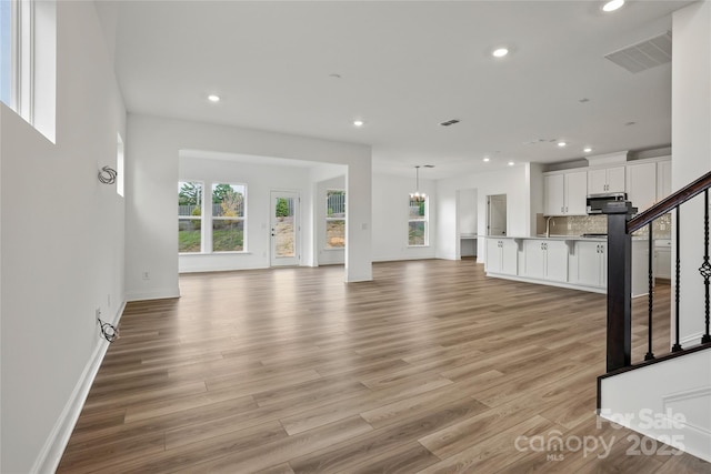 unfurnished living room with recessed lighting, visible vents, plenty of natural light, and stairs