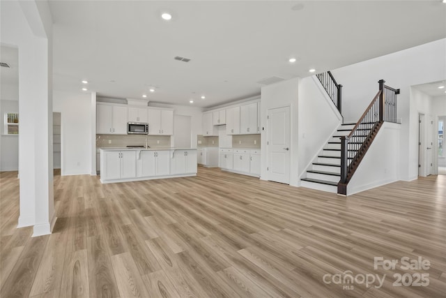 unfurnished living room with stairway, recessed lighting, visible vents, and light wood-style floors