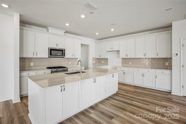 kitchen with a center island with sink, visible vents, stainless steel appliances, white cabinetry, and a sink