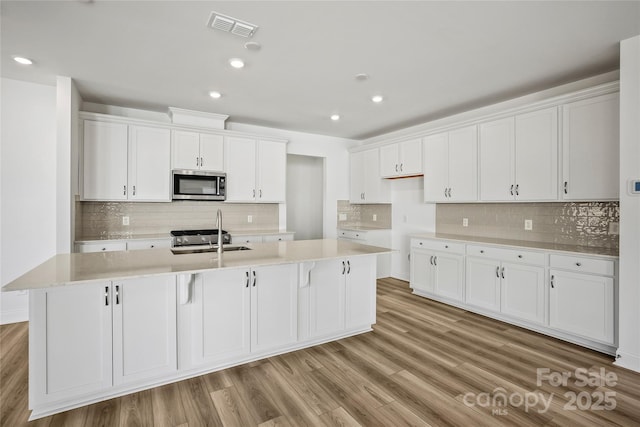 kitchen with white cabinetry, visible vents, stainless steel microwave, and a sink